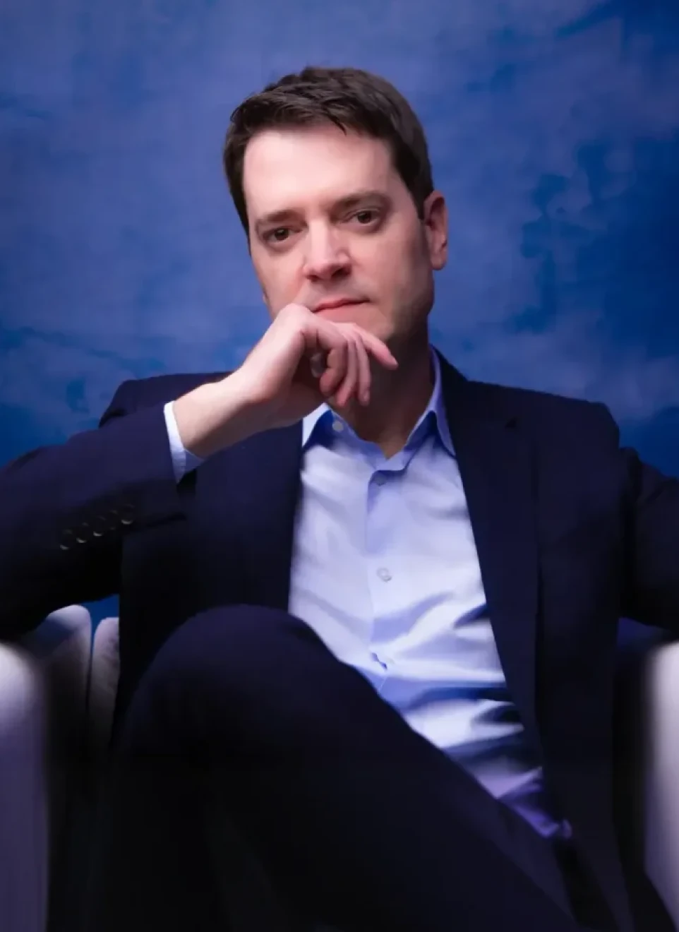 Dr. Eric Rulli sentado, apoiando o queixo na mão, vestindo terno azul-marinho