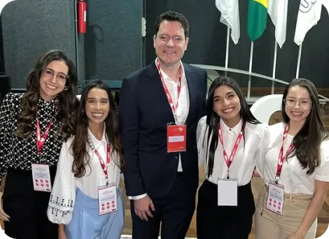 Dr. Eric Rulli posando com quatro colegas em evento médico, com bandeiras ao fundo